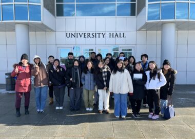 Photo of Apex for Youth students standing in front of a SUNY Albany campus sign, smiling and posing for a group picture