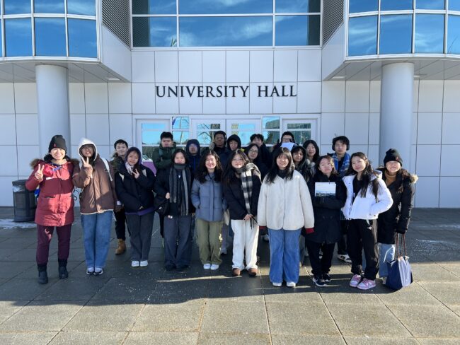 Photo of Apex for Youth students standing in front of a SUNY Albany campus sign, smiling and posing for a group picture